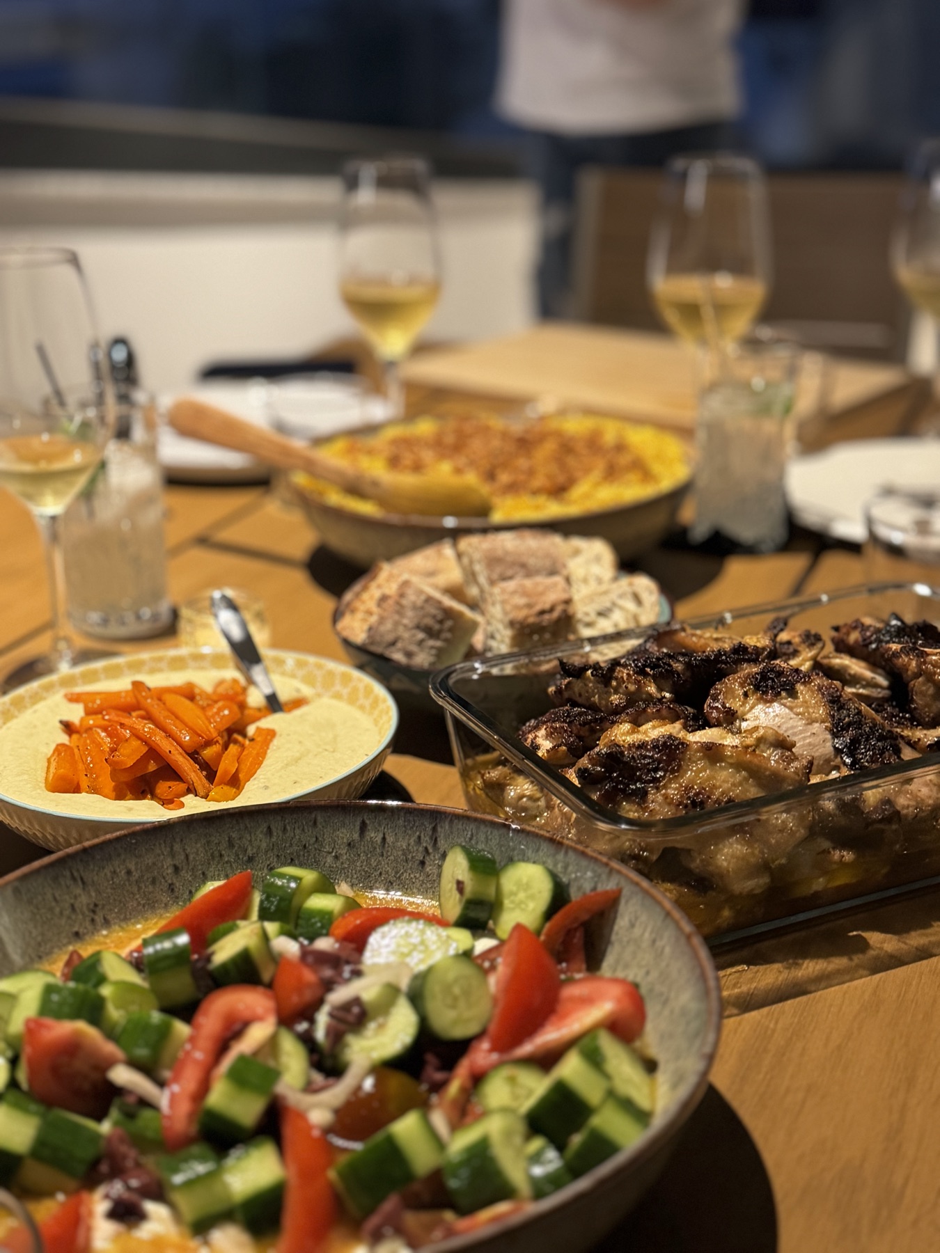 A dinner table with salad, roast chicken, bread and hummus